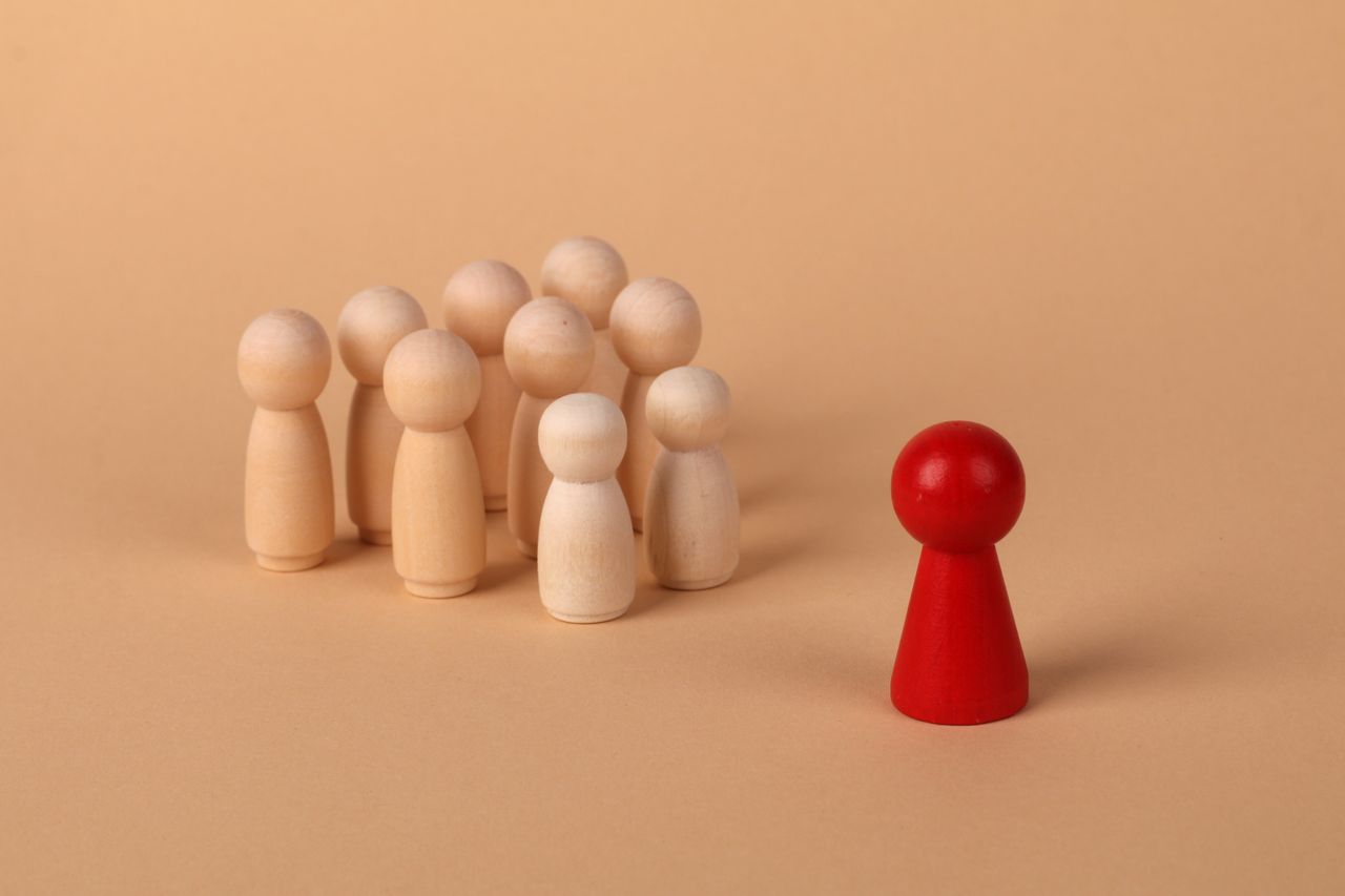 Red pawn standing apart from a group of wooden pawns symbolizing uniqueness and leadership.